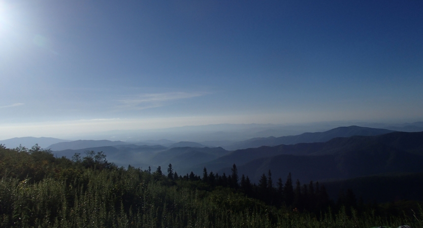 Under a blue sky, there is a mountainous landscape and green trees.